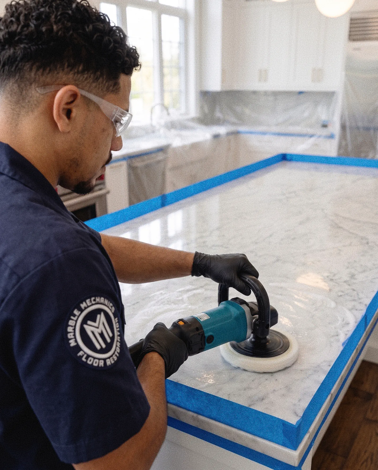 Stone restoration in Tampa Bay: a Marble Mechanics technician polishing a marble countertop with a rotary polisher, the edges masked off