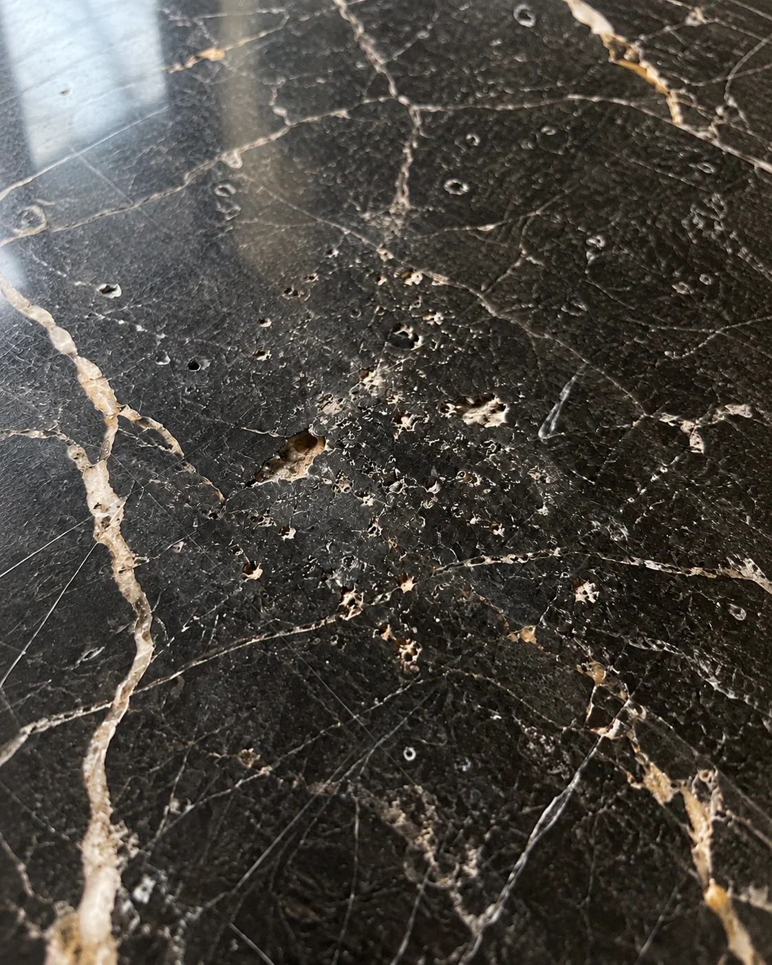 Heavily pitted and scratched black marble tile before repair by Marble Mechanics in Tampa Bay