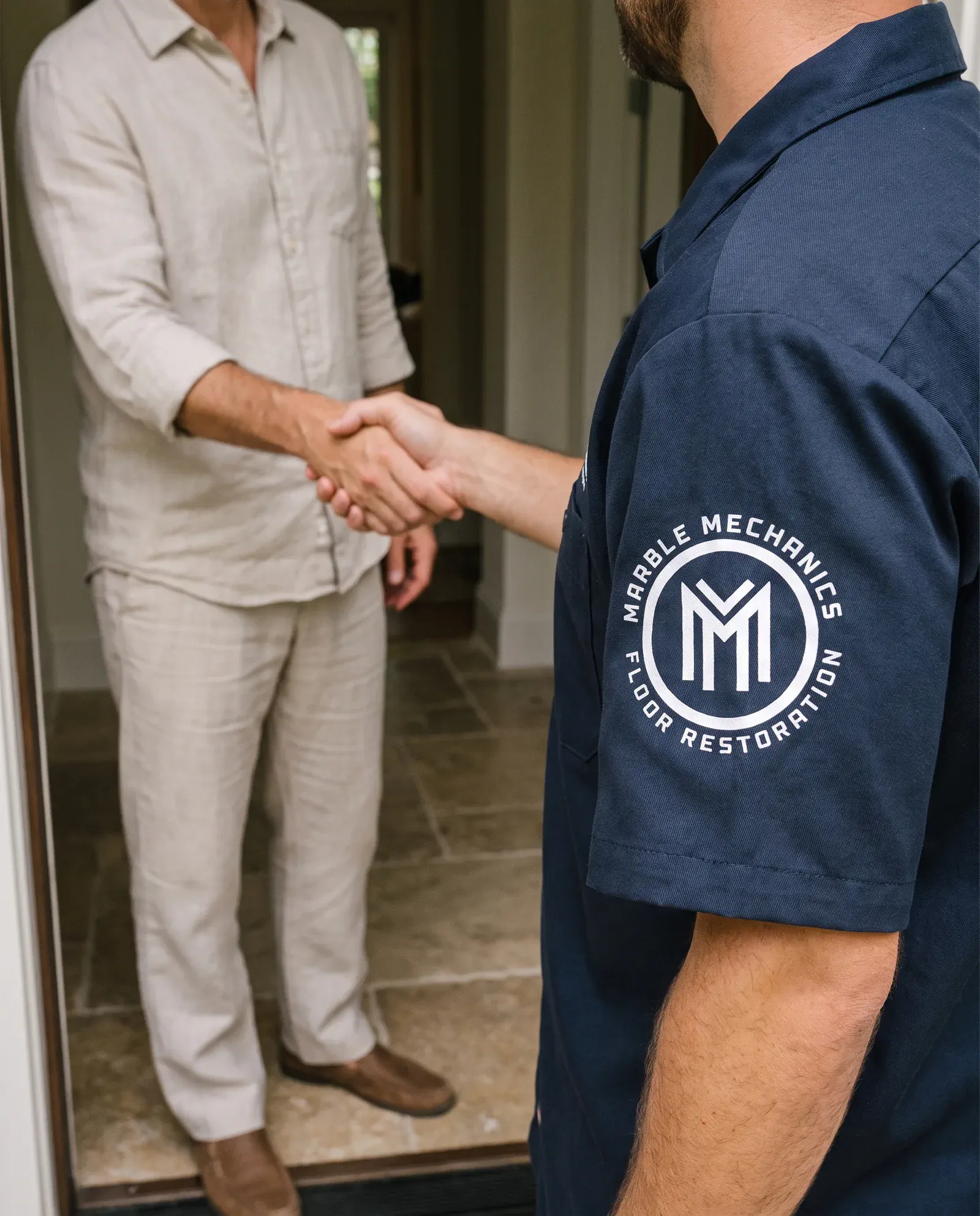 A Marble Mechanics technician in a navy branded shirt shaking hands with a homeowner at the front door after a free on-site estimate